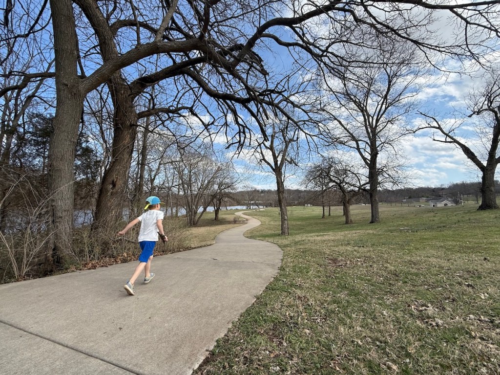 A paved trail winds through trees and a gentle rolling landscape.